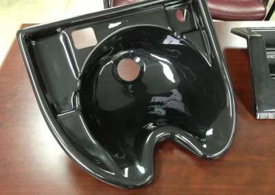 A glossy black molded salon shampoo bowl with a center drain hole and front neck cutout, sitting on a wood table.