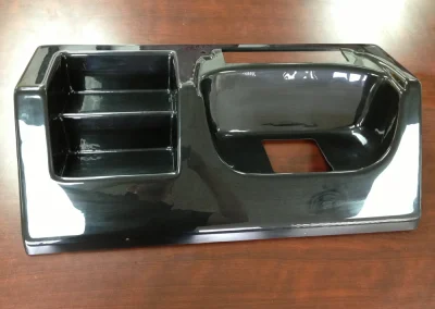 A glossy black molded salon station or console with a divided storage tray on the left and a recessed basin with a drain cutout on the right, on a wood table.