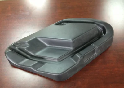 A black molded plastic enclosure or housing with a raised central section and contoured edges, sitting on a wood conference table.