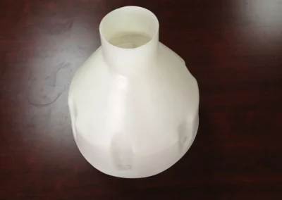 A white molded plastic tank or vessel with a narrow cylindrical neck and rounded contoured body, sitting on a dark wood table.