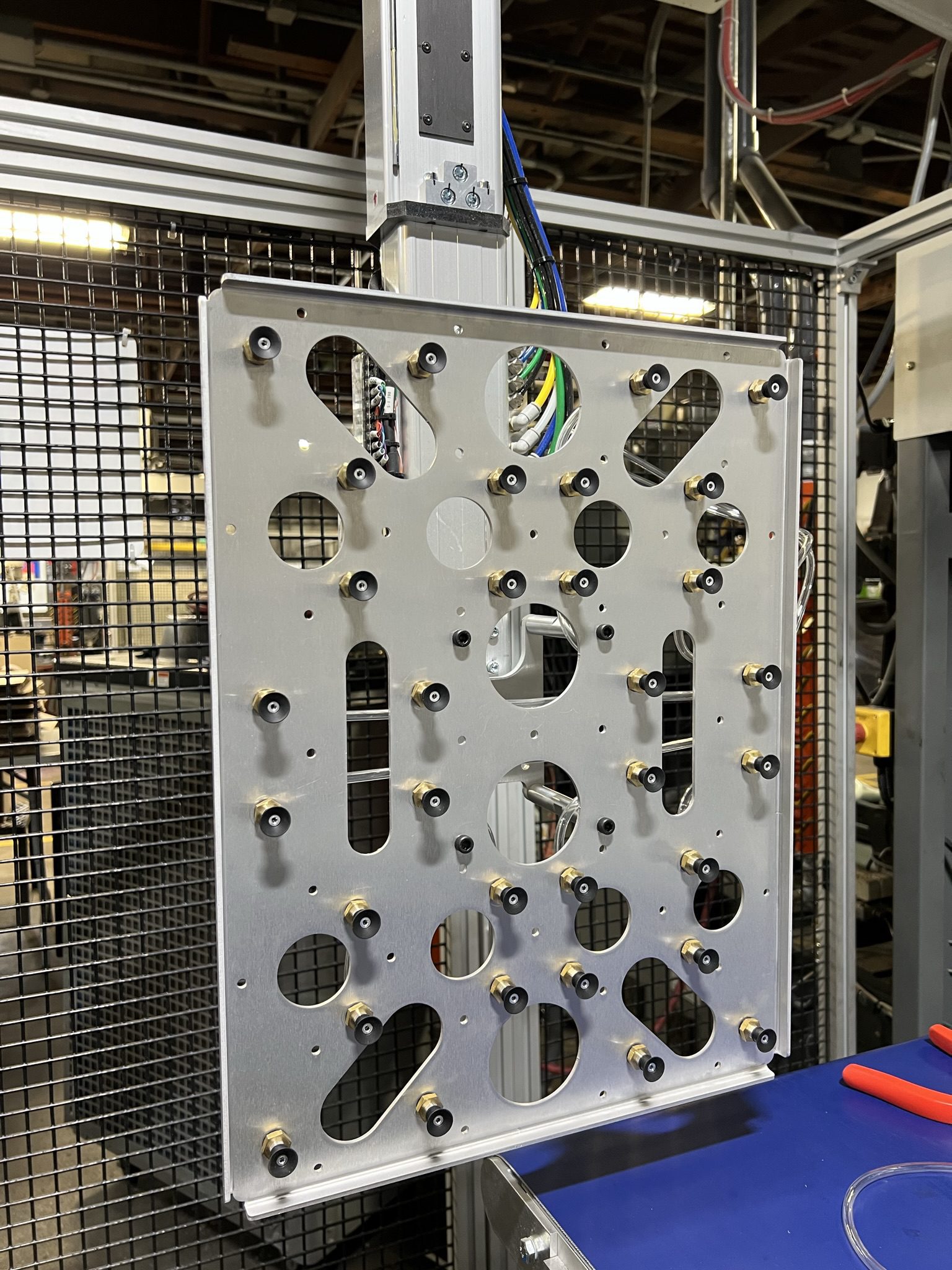 A robotic end-of-arm tooling (EOAT) plate mounted on a vertical axis inside a safety-guarded manufacturing cell, fitted with multiple vacuum suction cups and pneumatic fittings for part handling.