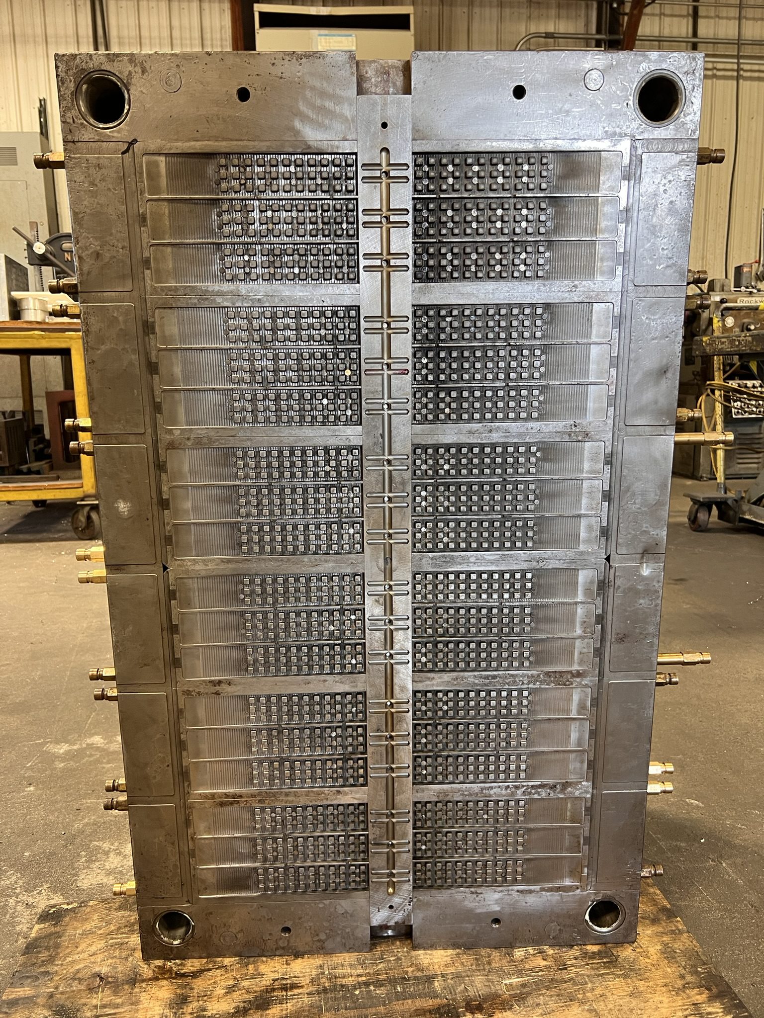 Large high-cavity injection mold tool standing open on a factory floor, showing both halves with densely patterned cavity arrays and a central runner system.