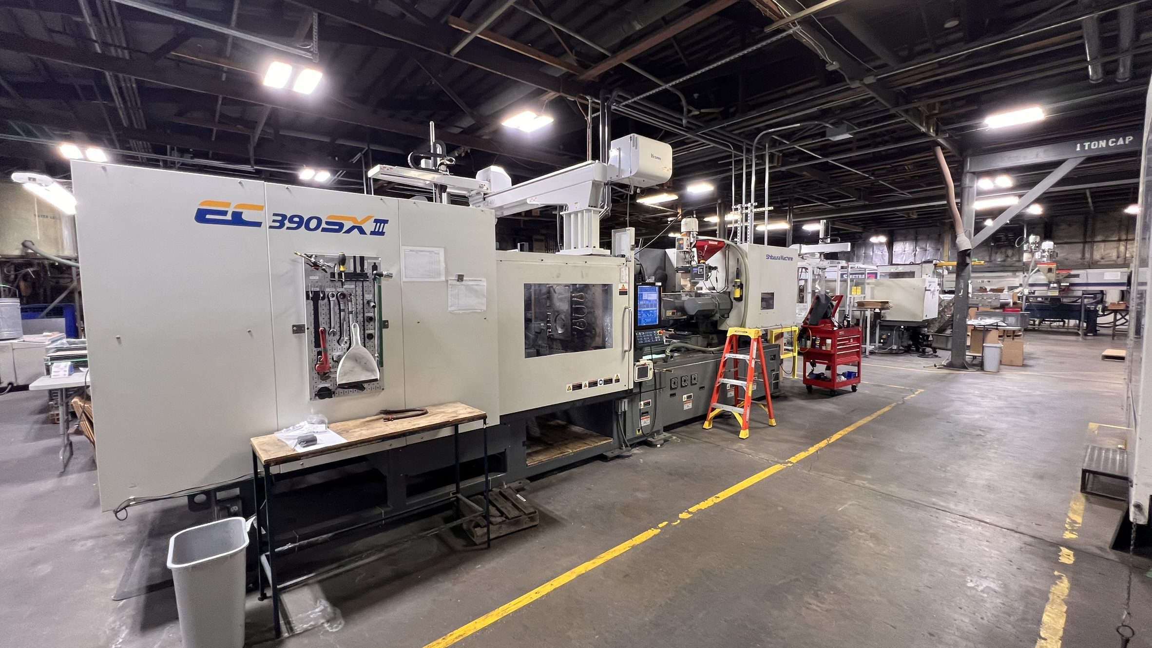 A Toshiba EC390SX III all-electric injection molding machine on a production floor, with additional injection molding machines visible in the background.