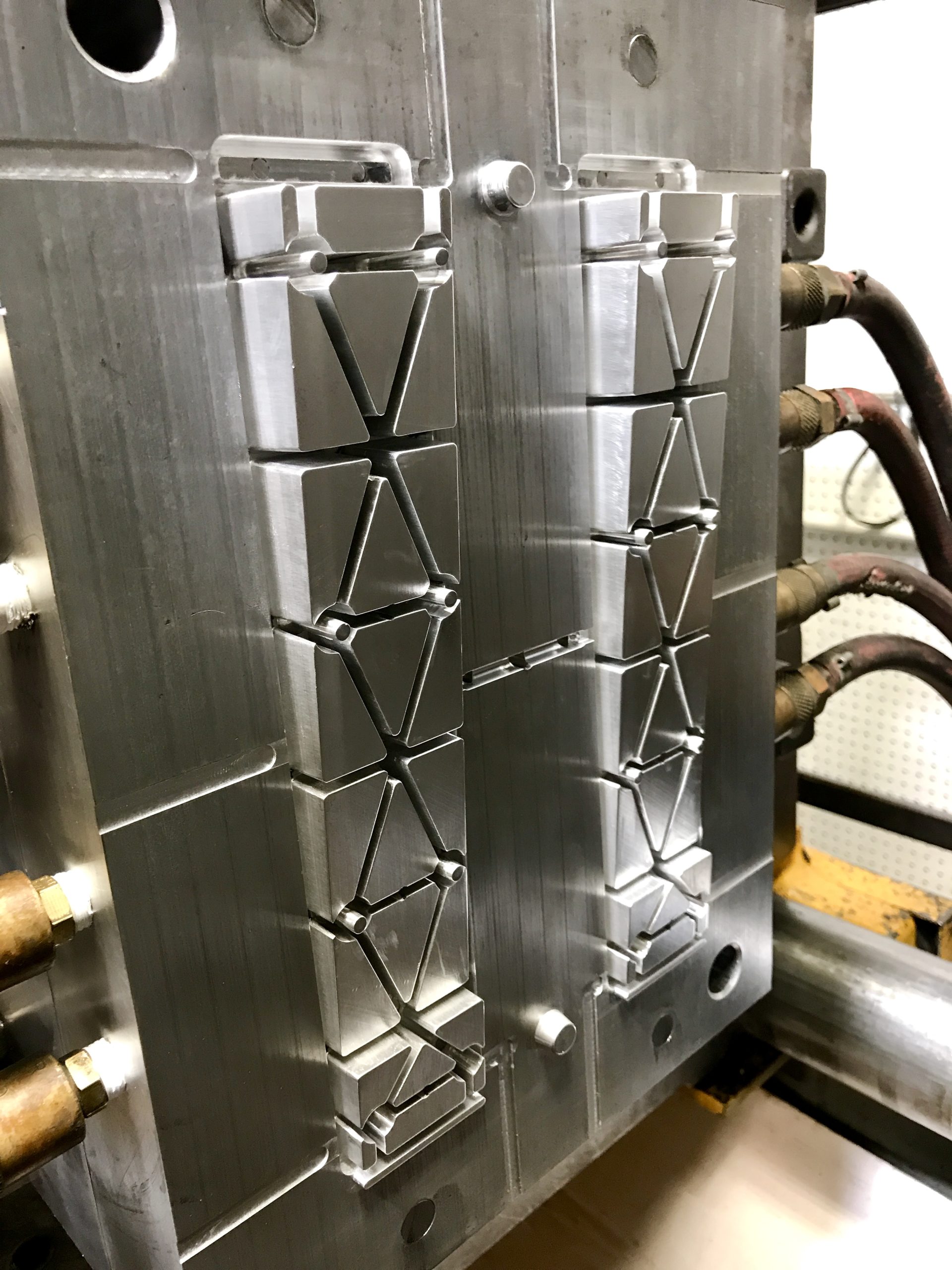 Close-up of an open multi-cavity injection mold showing machined steel tool halves with runner channels and gate systems, with hydraulic hoses visible in the background.